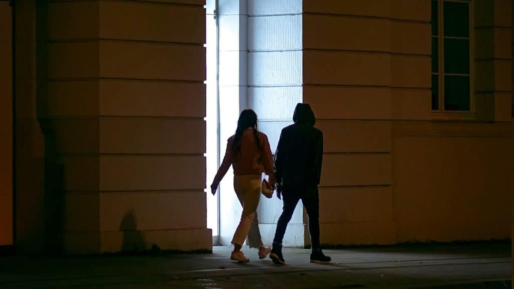 A woman leading a man while they walk down a street.