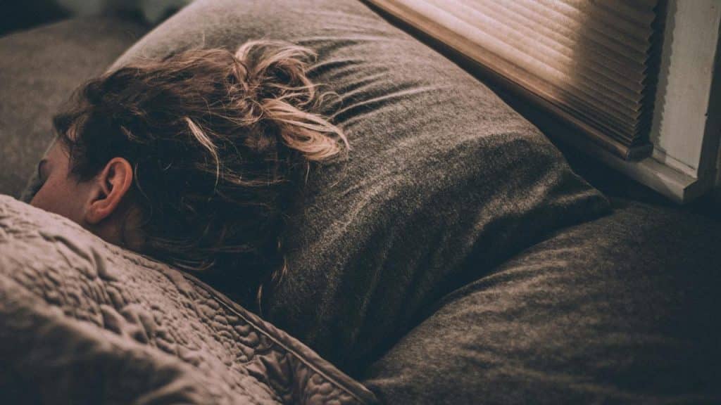 A person sleeps in bed with their head resting on a dark pillow.