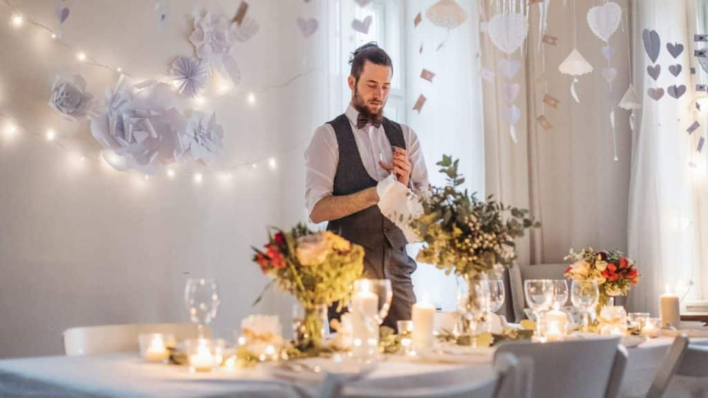 A man in formal wear stands looking down at a decorated table set for a celebration.