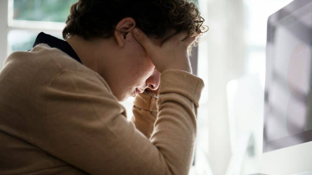 A person sits slumped over with hands pressed to their temples in distress.
