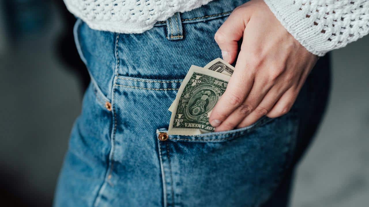 A person’s hand placing dollar bills into a jeans pocket.