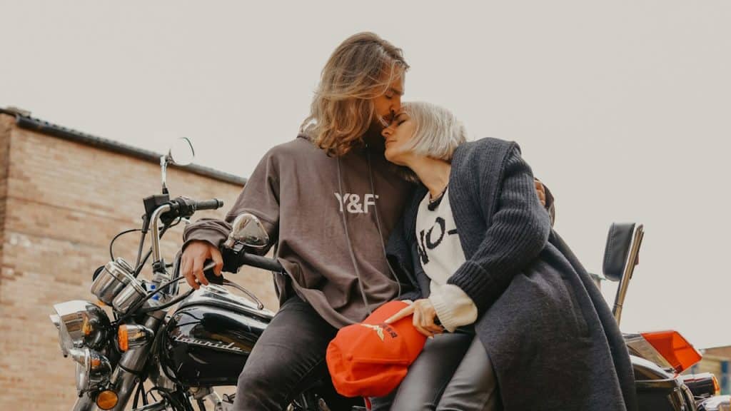 A man kissing a woman’s forehead while sitting on a motorcycle.