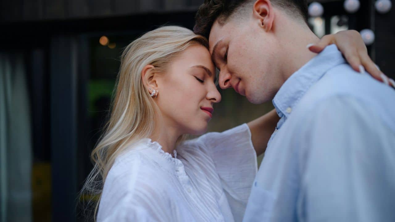 A young couple is embracing, forehead to forehead, with their eyes closed.