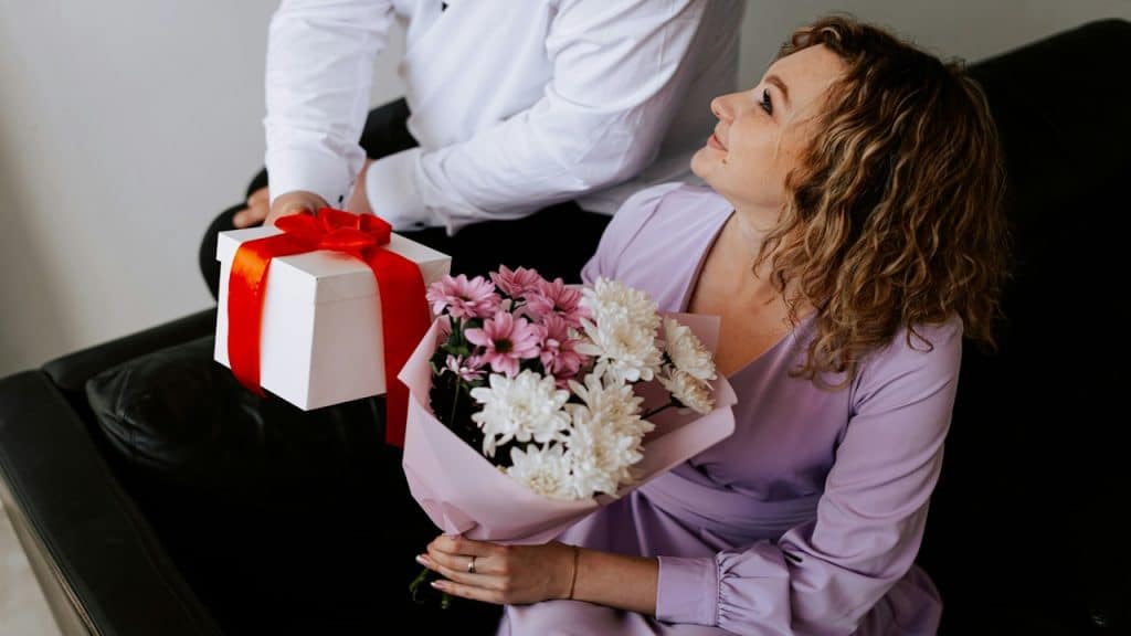 A man giving a present and a bouquet of flowers to his wife.