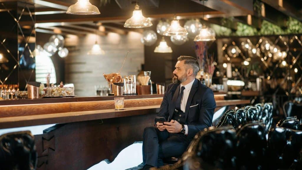 A man in a suit sitting alone at a bar with a drink.