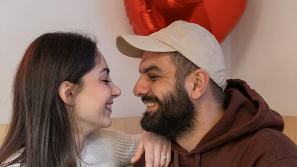 A smiling man and a woman sitting next to each other with a red balloon in the background.