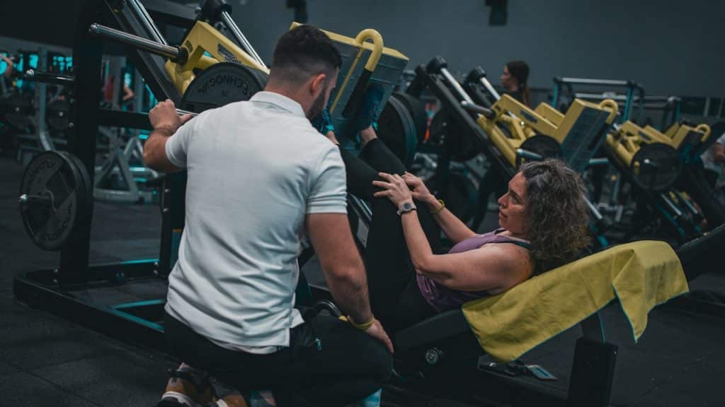 A woman doing leg presses in the gym while a man supervises.