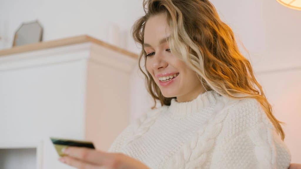 A smiling woman holding a credit card indoors.