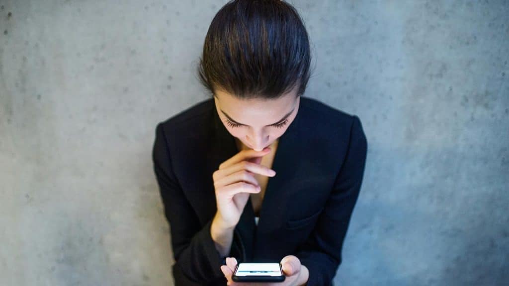 A woman in a dark blazer looking down at her phone thoughtfully.