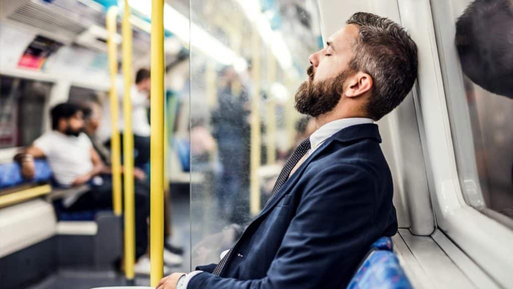 A man in a suit sleeping on a subway train.