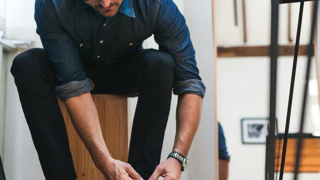 A man sitting on a stool and bending down to tie his shoe.