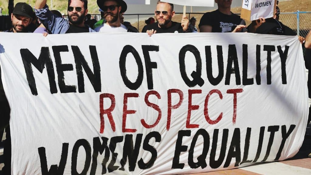 Men holding a women's equality banner on the road.