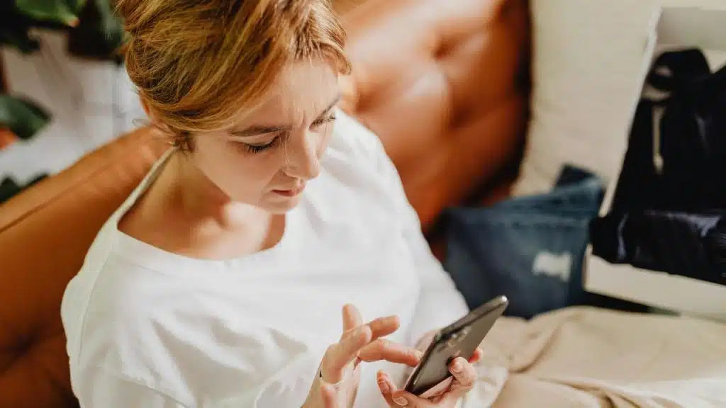 A woman sitting on a couch looking at her smartphone.