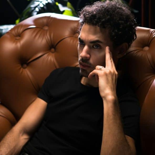 Pensive man with dark, curly hair sitting in a brown leather armchair.