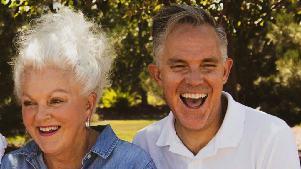 An elderly couple is sitting in a park and smiling together.