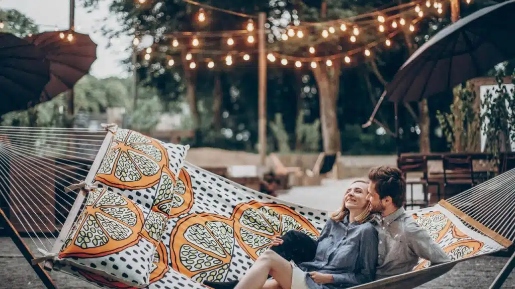 A couple relaxing together on a colorful hammock under string lights outdoors.