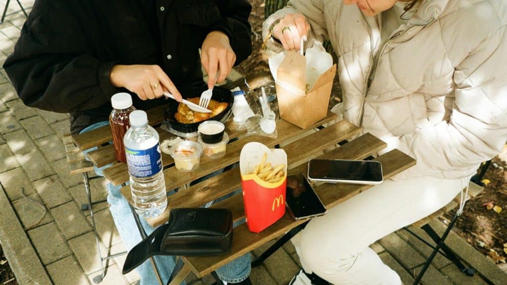 A couple eating fast food at an outdoor table with drinks and fries.