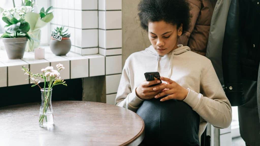 A person in a light hoodie sits at a cafรฉ table looking at their phone.