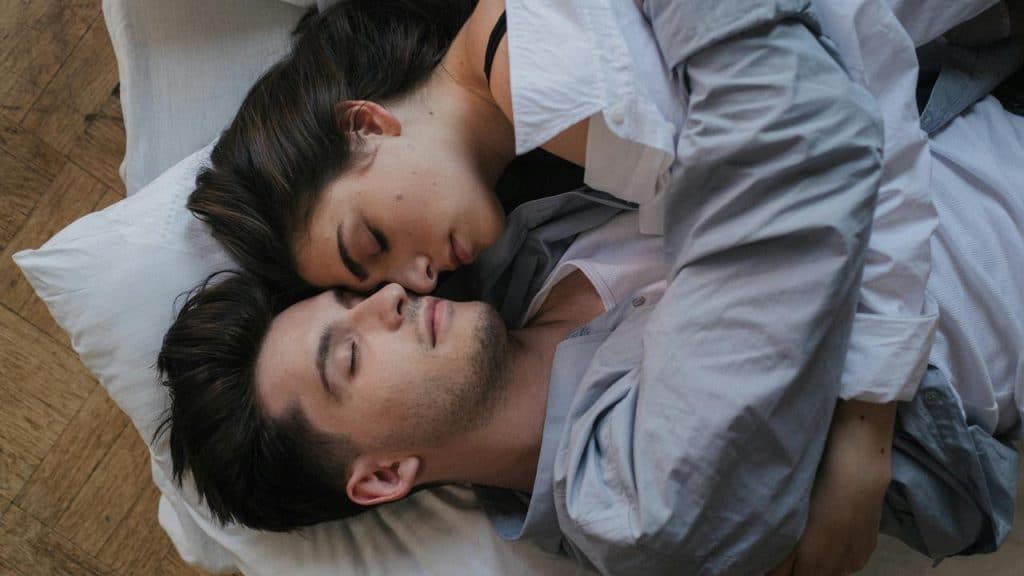 A couple lying close together in bed, resting peacefully.