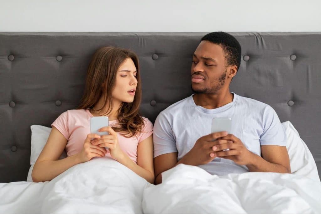 A man and woman at the bed using their phones