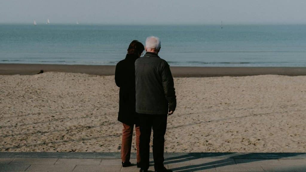 A couple standing on the beach besides the sea.