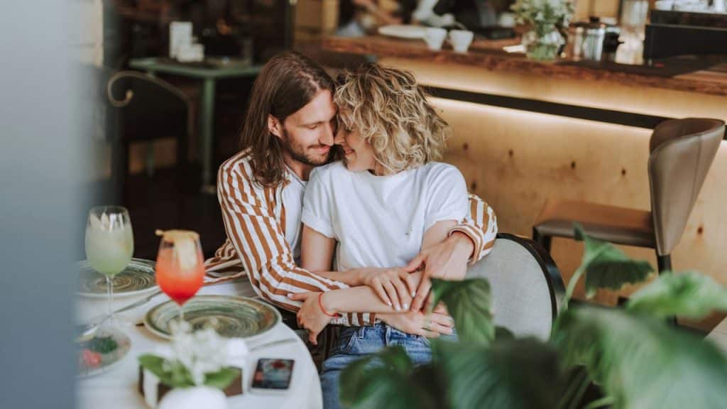 Man embracing a smiling woman from behind in a restaurant setting.