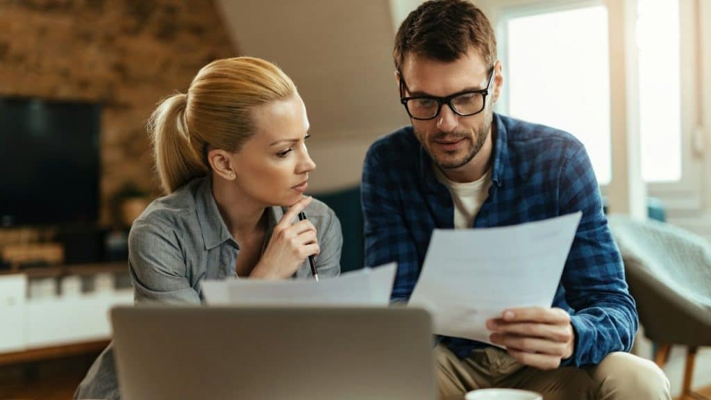Man and woman sitting together reviewing documents in a living room with a laptop.