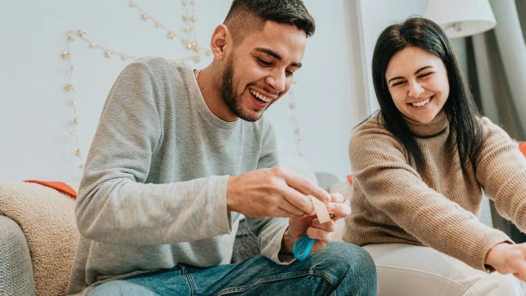 A man and woman laughing while crafting together indoors.