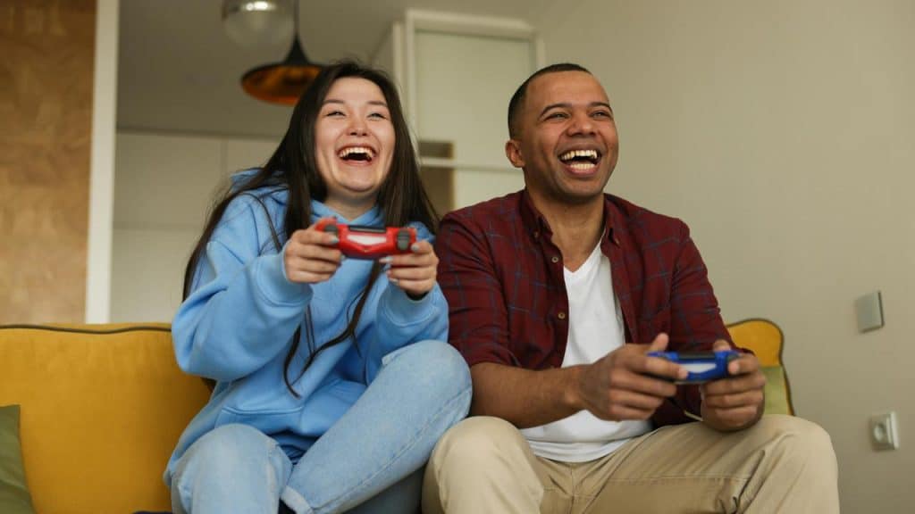 A couple laughing together while playing video games on the couch.