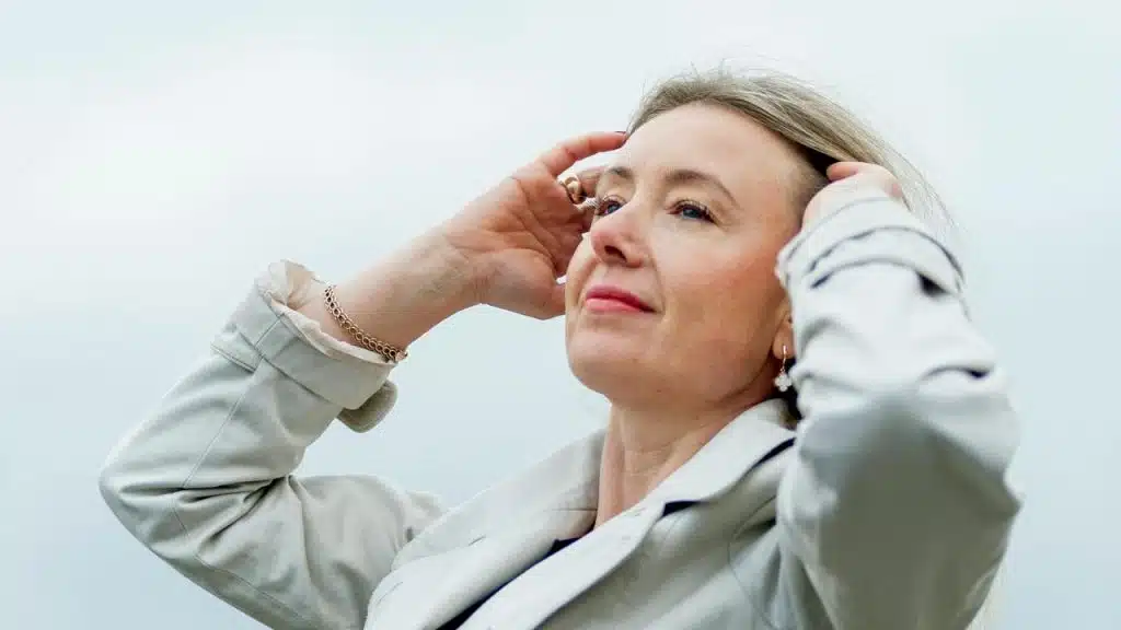 A woman looking upward with her hands in her hair.