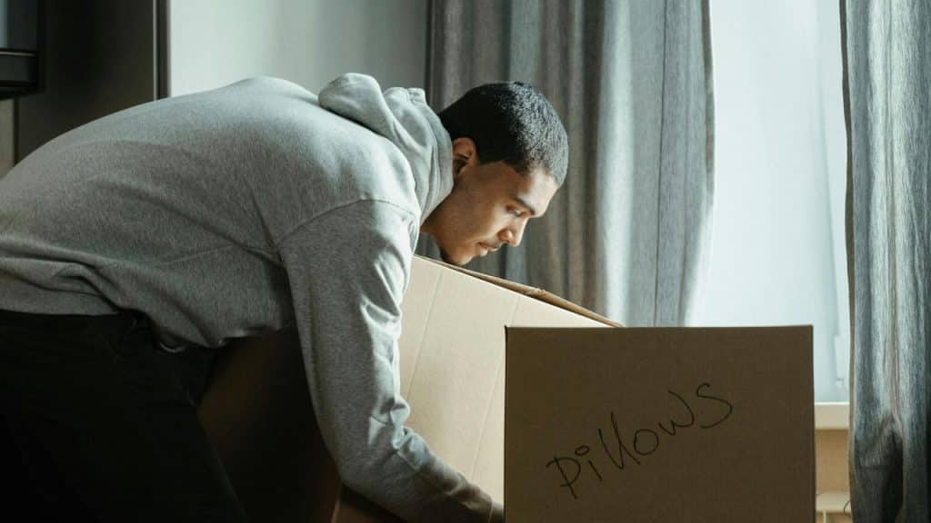 A man leaning over a cardboard box labeled “pillows” while unpacking.