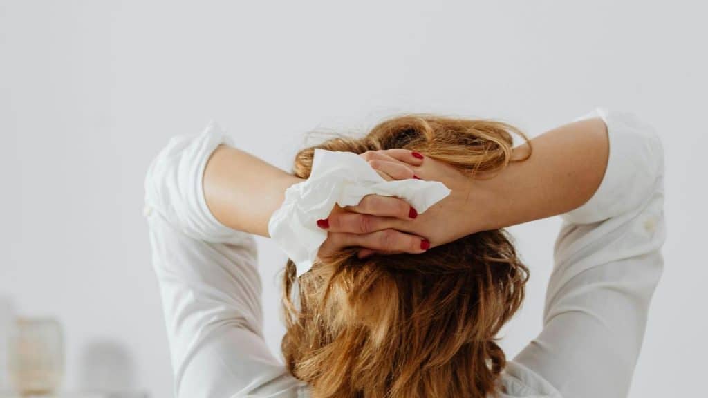 A person sitting with their hands behind their head holding a tissue.
