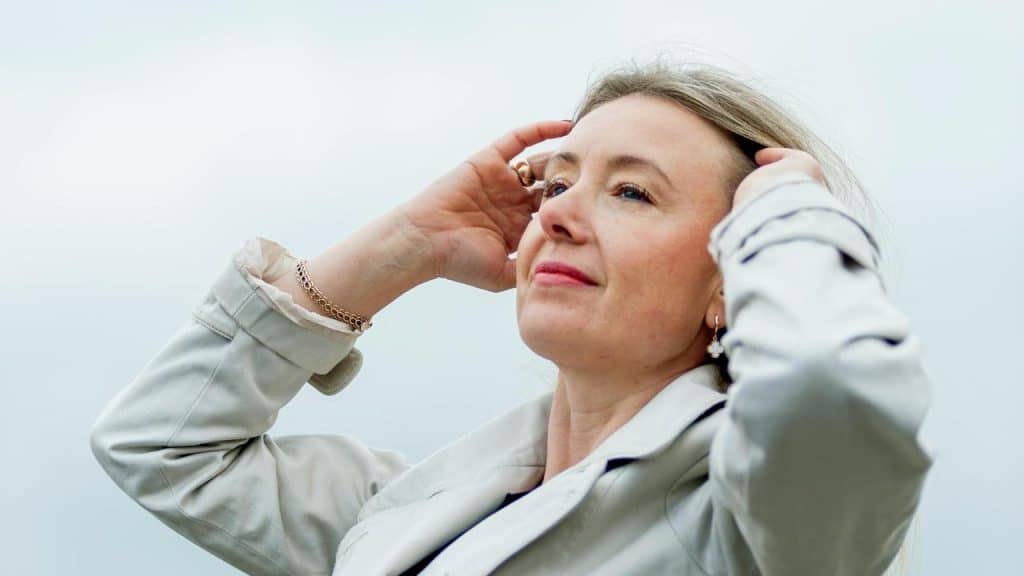 A woman looking upward with her hands in her hair.