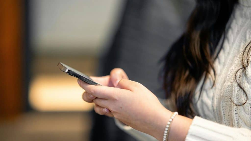 A woman holding a smartphone while wearing a white sweater.