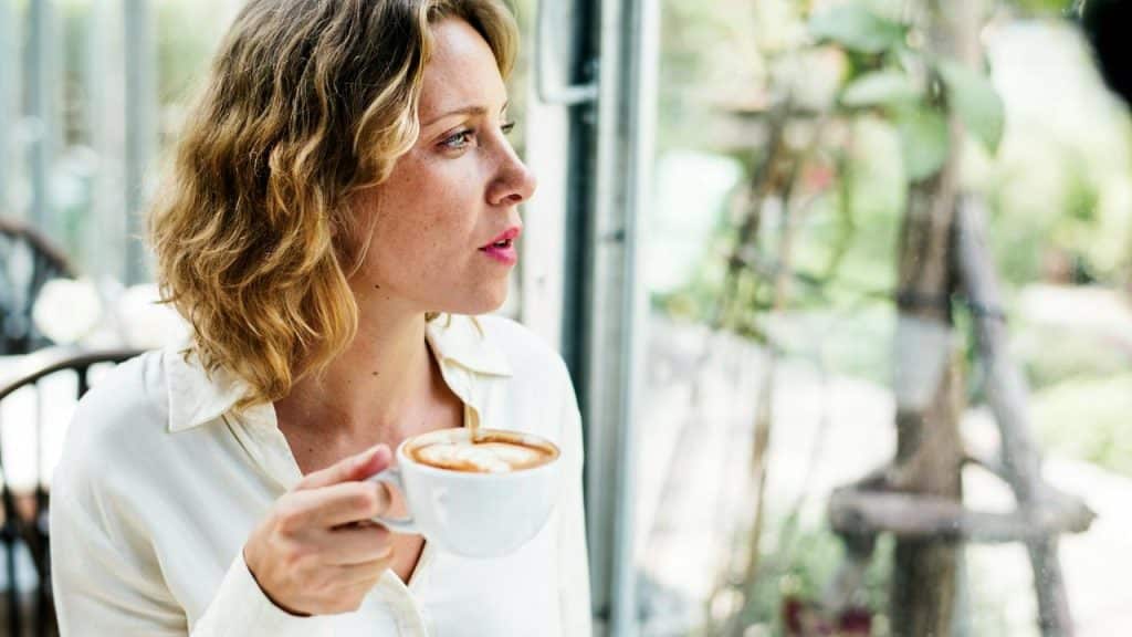 A woman holding a cup of coffee while looking out the window.