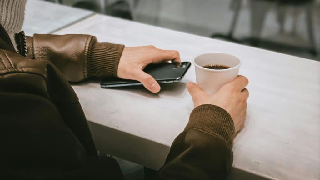 A person holding a cup of coffee in one hand and a smartphone in the other.