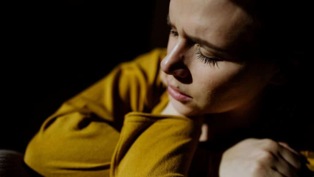 Close-up of a woman in a yellow shirt with her eyes closed in shadow.
