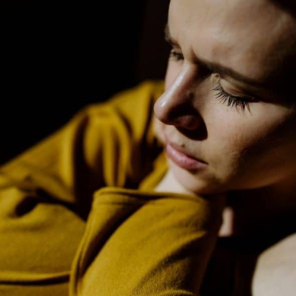 Close-up of a woman in a yellow shirt with her eyes closed in shadow.