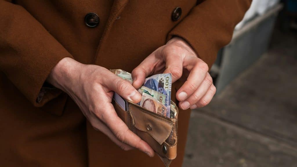 A person in a brown coat is holding a wallet full of money.