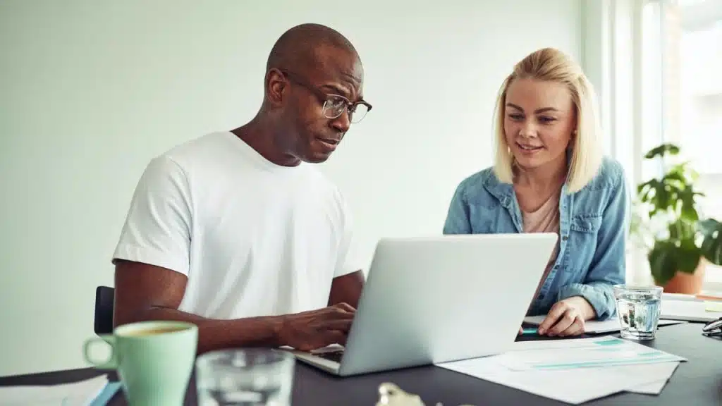 Two people looking at a laptop together at a table with coffee and water.