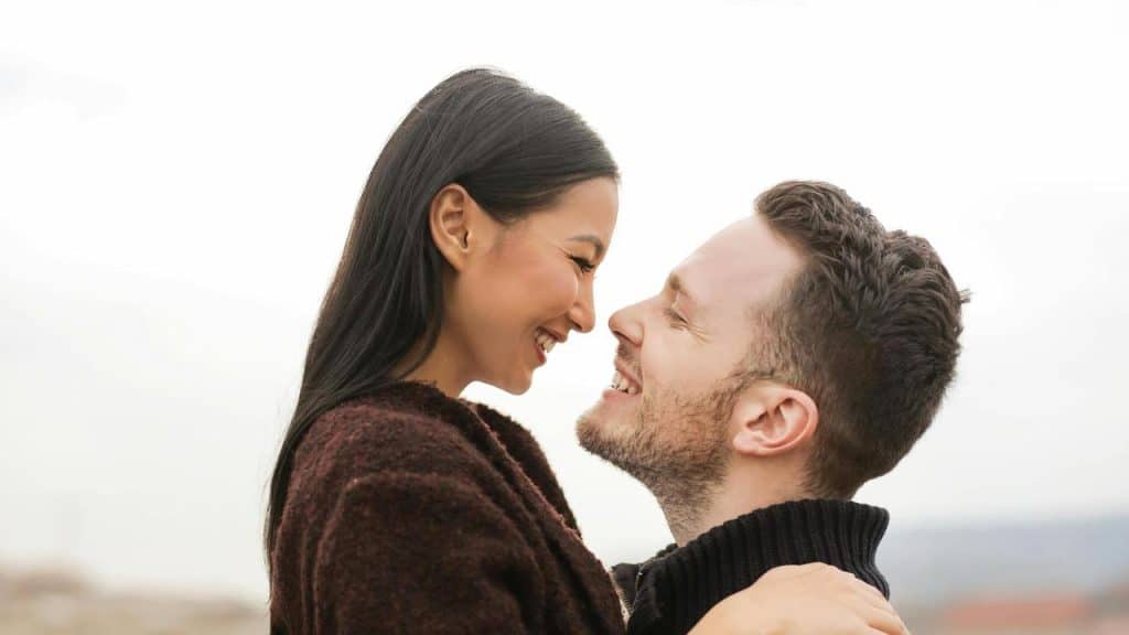 A couple smiling closely as they hold each other outdoors.