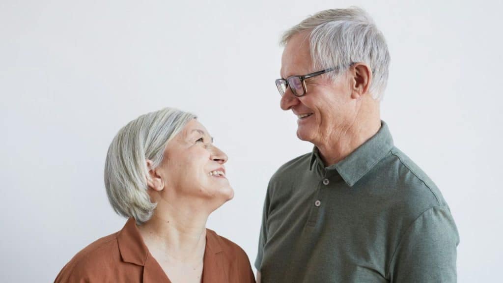 Smiling elderly woman in brown top looking up at a smiling elderly man in glasses.