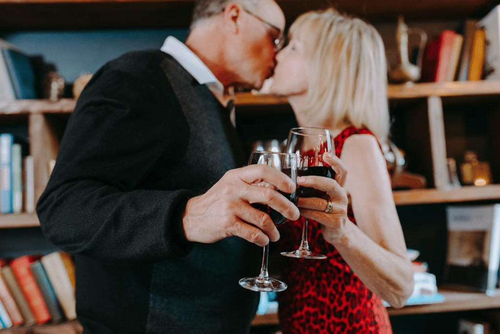 Photo of an Elderly Couple Kissing while Holding Glasses of Wine