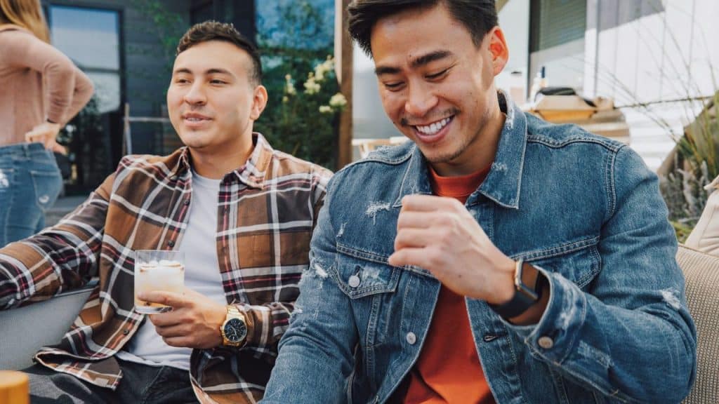 Two casually dressed men smiling and socializing outdoors, one holding a drink.
