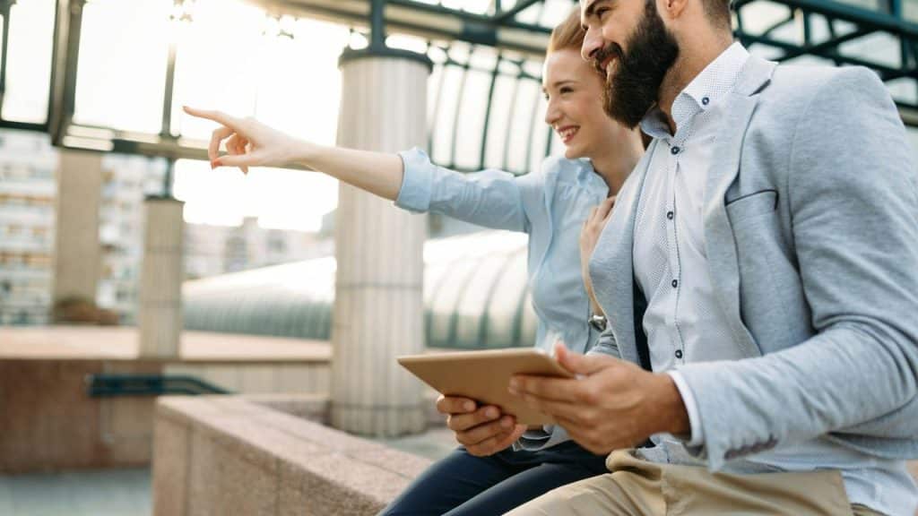 A smiling woman pointing while sitting beside a man holding a tablet.