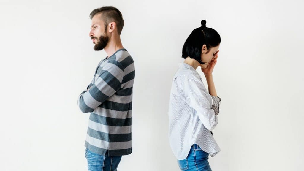 A couple standing with their backs to each other and refusing to talk while the woman holds her hand to her face.