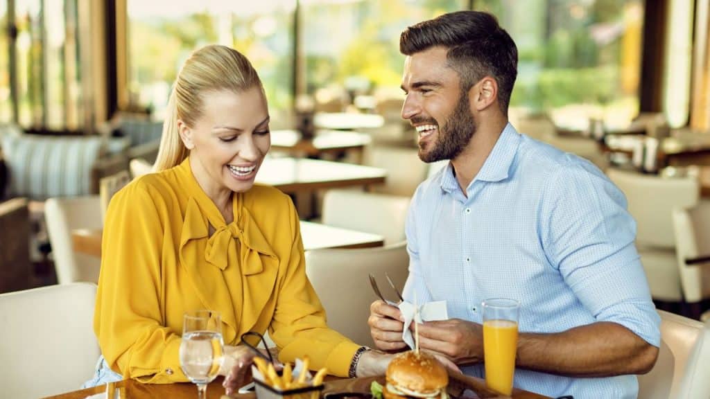 A man and woman are smiling and laughing together at a restaurant table.