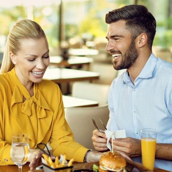 A man and woman are smiling and laughing together at a restaurant table.