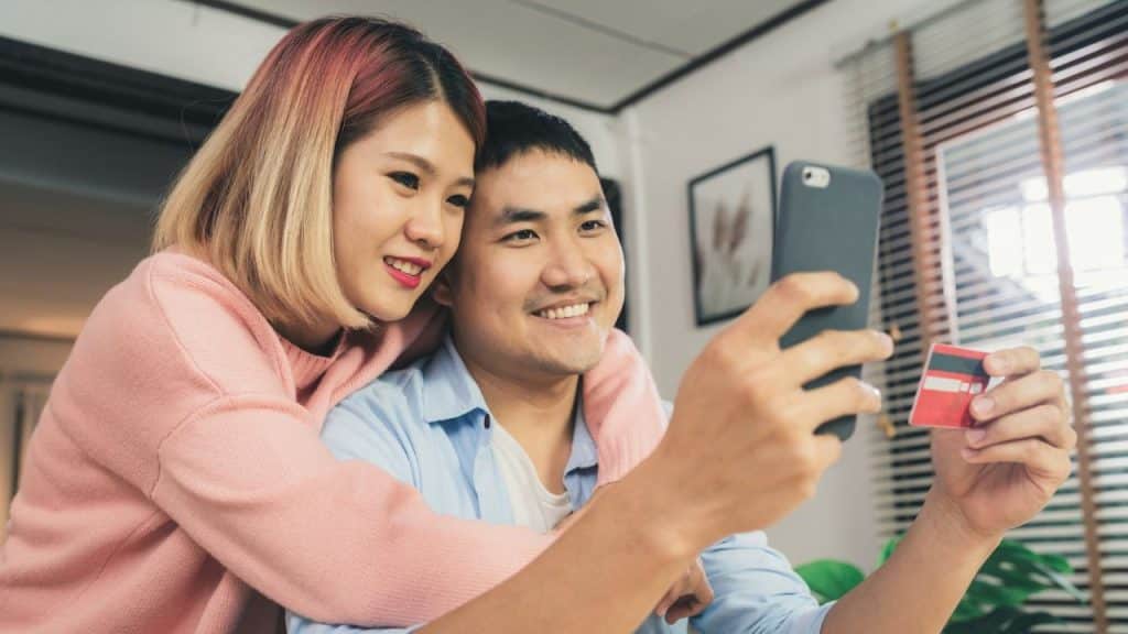 A smiling couple looks at a smartphone as the man holds a credit card.