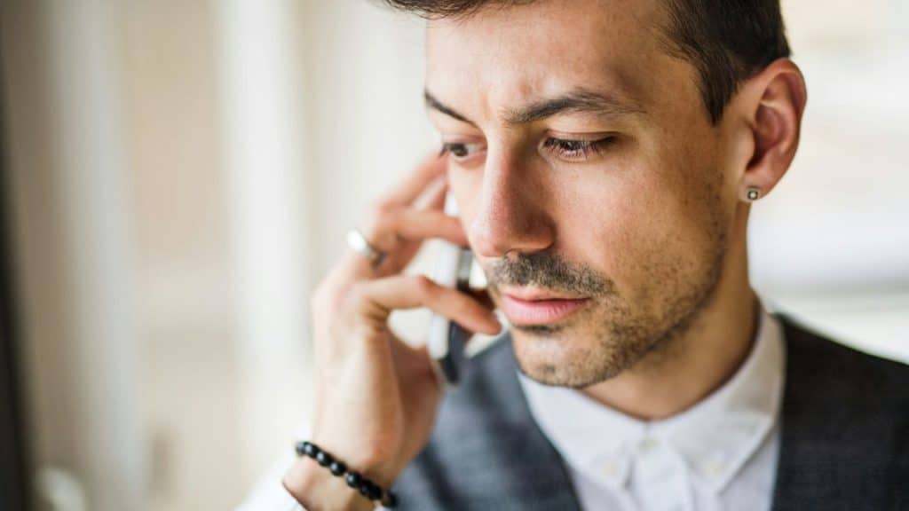 Close-up of a man in a vest and white shirt on a phone call with a serious expression.